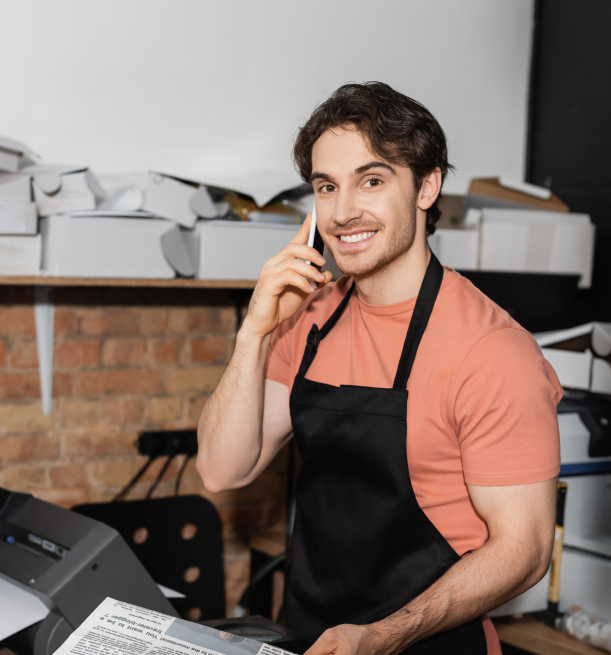 a male business owner wearing a salmon colored shirt and an apron is on the phone with his attorney