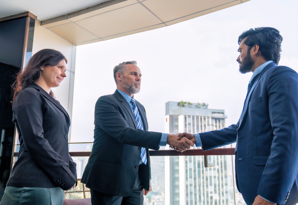 two parties involved in a corporate merger shaking hands on a building balcony