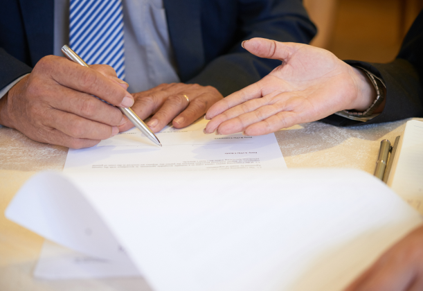 a business owner signing a government contract while attorney is explaining to him the details